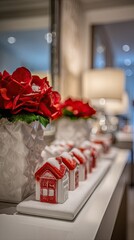 Festive miniature houses with snowy roofs are displayed on a white tray, alongside a vibrant poinsettia, creating a wintery holiday scene.