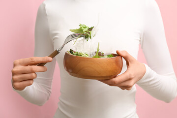 Woman holding bowl of salad with plastic on pink background, closeup. Microplastic Awareness Month