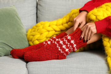 Woman in red knitted socks with blanket sitting on sofa at home, closeup