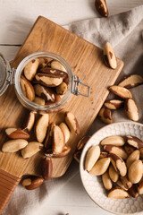 Bowl and jar with tasty Brazil nuts on white wooden background