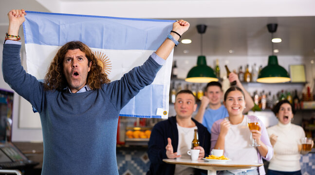 Company of joyful fans of different ages waving flag of Argentina and celebrating victory of favorite team in sports bar - Powered by Adobe