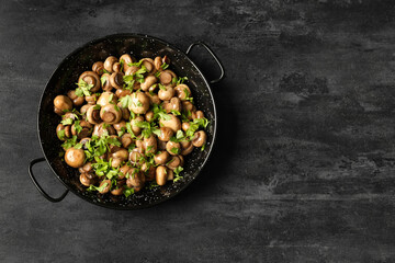 Frying pan with roasted mushrooms and parsley on black background