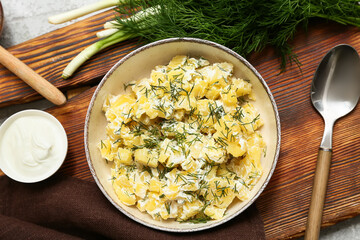 Bowl of tasty potato salad with dill, green onion and sour cream on wooden board