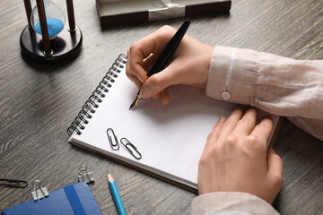Female hands with blank notebook, fountain pen, stationery and hourglass on wooden table, closeup