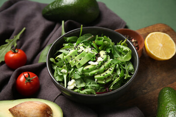 Bowl with tasty avocado salad with mozzarella cheese and ingredients on green background