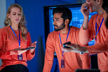 A data analytics team in a command center reviews a live security feed on a mobile device. They are collaborating on a strategy to respond to a new threat on the network.