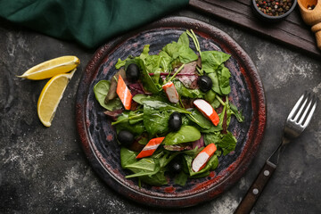 Plate of salad with crab sticks, spinach, black olives and ingredients on grey grunge background © Pixel-Shot