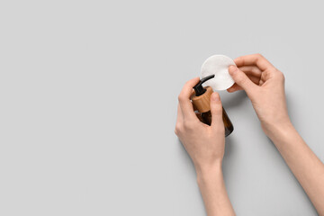 Beautiful female hands with bottle of cosmetic product and cotton pad on grey background © Pixel-Shot