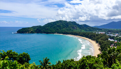 Panoramic view of a stunning tropical bay with turquoise ocean, sandy beach, lush green mountains, and a coastal town under a cloudy blue sky. Idyllic vacation destination.