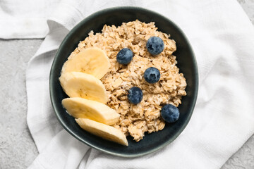 Bowl with tasty oatmeal, berries and banana on grey grunge background