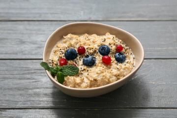 Bowl with tasty oatmeal and berries on grey wooden background