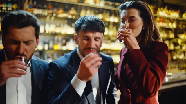Emotional coworkers drinking shots in golden light bar closeup. People toasting