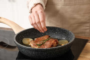 Woman frying tasty steak in kitchen