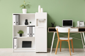 Interior of stylish office with modern water cooler, workspace and shelving unit