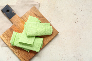 Wooden board with rolled green lavash on white grunge background