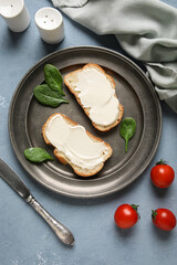 Plate of tasty bruschetta with processed cheese, spinach leaves and fresh tomatoes on blue background. Top view