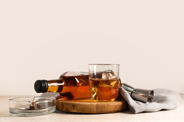 Bottle, glass of cold rum and ashtray on table against white background. Closeup