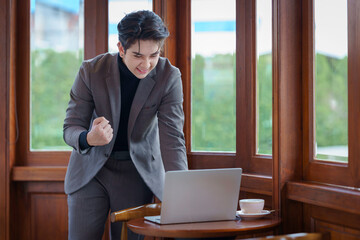 Excited businessman celebrating success while working on a laptop. Working online in a coffee shop.