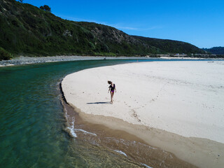 Aerial view of young beautiful woman walking on the sandy beach next to next to river on ''Praia da Amoreira'' in Portugal. Fashion model is enjoying traveling.