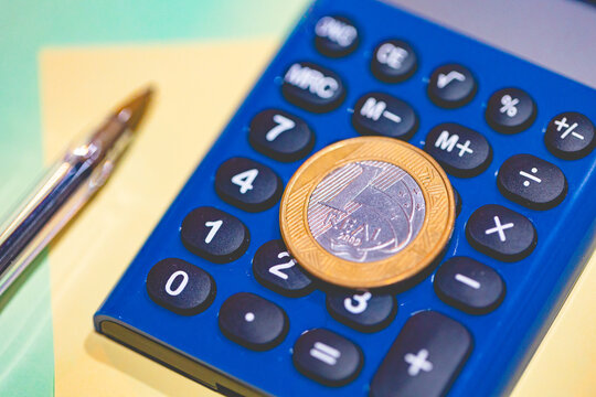 Brasil - Economia e Finan&ccedil;as. Uma moeda de 1 Real sobre uma calculadora azul. Crise, Infla&ccedil;&atilde;o, Imposto de Renda, taxa&ccedil;&atilde;o, tarifa.