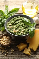 Fresh pesto sauce in bowl and ingredients on wooden table, closeup