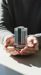 Hands holding miniature modern building, symbolizing real estate investment, property management, and urban development with sense of care and responsibility
