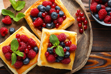 Tasty puff pastries with berries and mint on wooden table, flat lay
