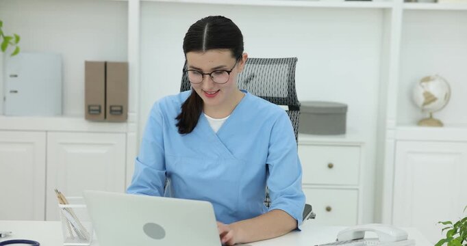 Nurse working with laptop at white table in clinic