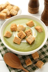 Tasty broccoli cream soup with croutons served on white wooden table, closeup