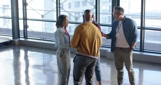 Diverse coworkers stepping forward for handshakes in atrium then viewing tablet discussing plan
