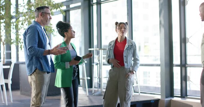 Diverse coworkers in co-working space explaining layout, welcoming newcomer entering, shaking hands
