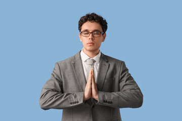 Young businessman meditating on blue background