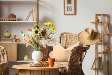Vase with autumn flowers and coffee cup on table in living room