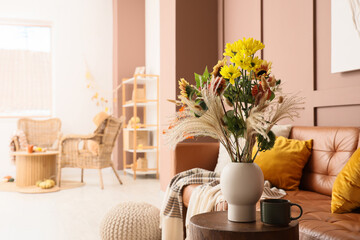 Vase with autumn flowers and cup of coffee on table in living room