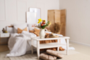 Blurred view of light bedroom with table and autumn flowers in vase