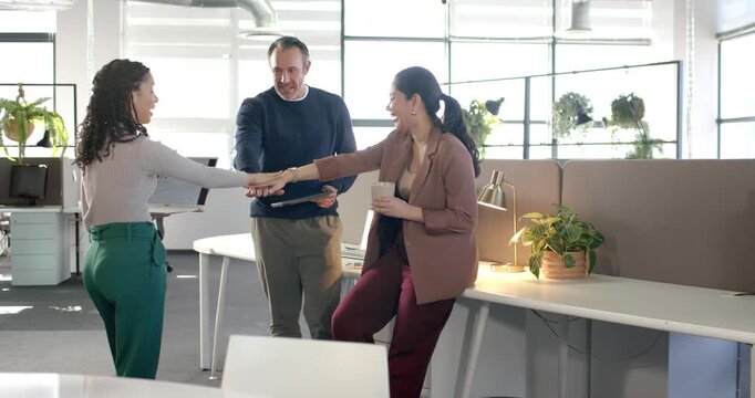 Diverse coworkers presenting tablet chart at desk celebrating growth by stacking hands overhead
