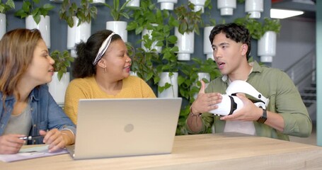 Picking up VR headset, man explaining design to diverse coworkers at coworking lounge, copy space