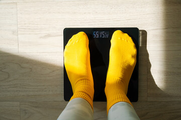 Woman standing on digital weight scale in yellow socks. Personal weight control and health...
