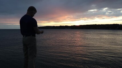 Middle-aged man taking a picture from his cell phone of the sunrise and captivating tapestry of colors over the water
