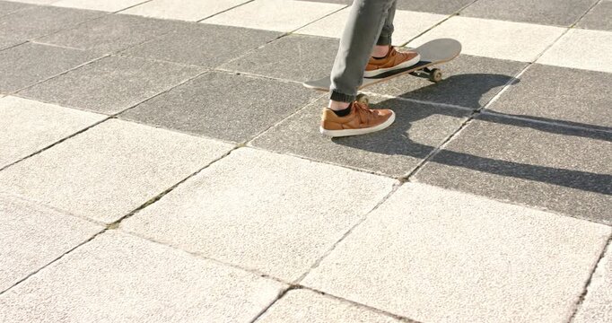 Male skateboarder placing front foot on sunlit urban plaza, pushing board to coast across tiles