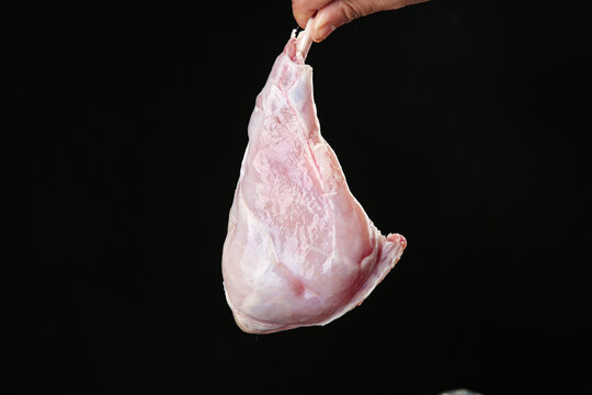 Raw Rabbit Foreleg Meat Cut Held by Hand on Black Background - Fresh Uncooked Protein for Cooking