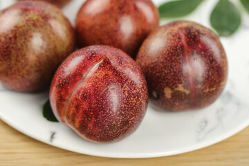 Fresh Ripe Red Purple Plums on White Plate with Green Leaves - Healthy Fruit Food Photography