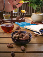 Dried Black Walnuts Falling Into Bowl with Herbal Tea and Natural Health Ingredients on Rustic Wooden Table