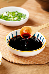 Dark soy sauce in bowl with wooden spoon and fresh herbs on bamboo placemat