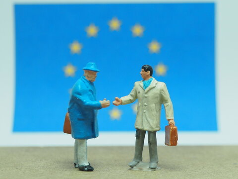 Mini toy of action figure at table with blurred background. Miniature photography concept. Businessman with European Union (EU) flag as a background.