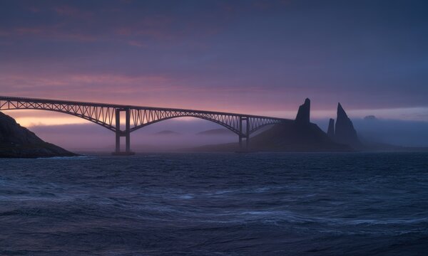 A dramatic bridge spans a misty sea at dawn