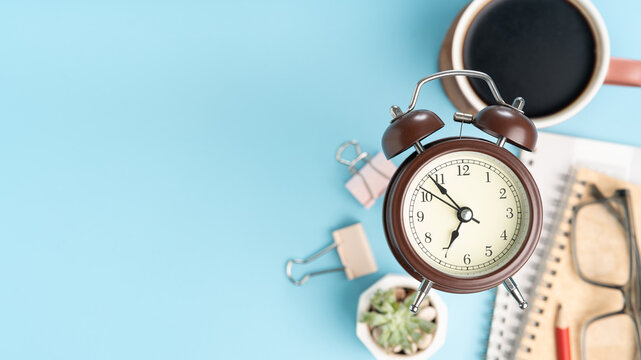 Start your day right with this cozy workspace scene featuring a retro clock, coffee, and stationery on a calming blue backdrop, perfect for productivity - Powered by Adobe