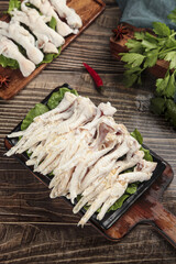 Fresh Raw Chicken Feet on Wooden Cutting Board with Herbs for Cooking Preparation