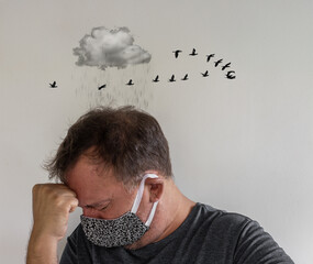 Adult male wearing a mask with head down and hand on forehead, surreal rain cloud and birds above