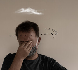 Adult male wearing a mask with eyes closed, touching his face in stress, with surreal birds